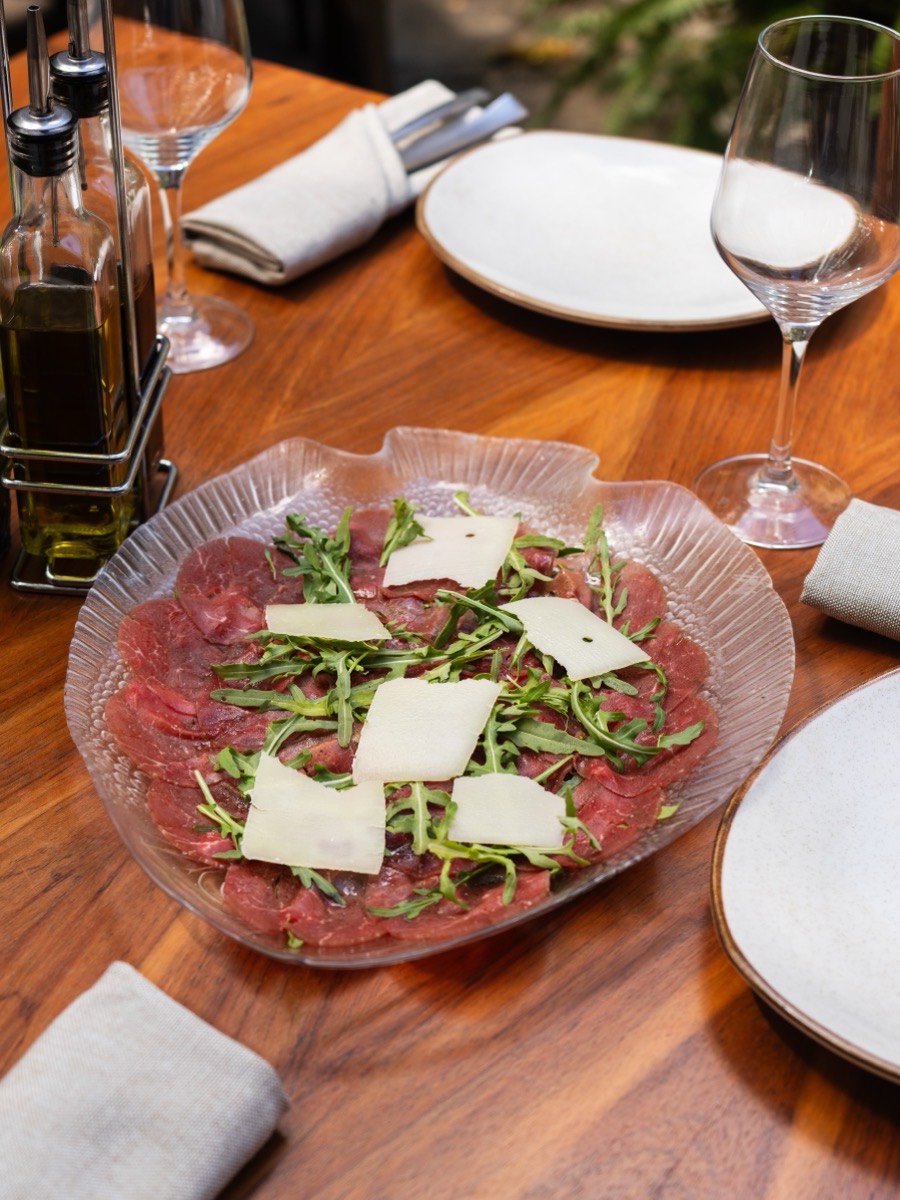 Beef carpaccio with arugula and shaved parmesan, on a glass plate.