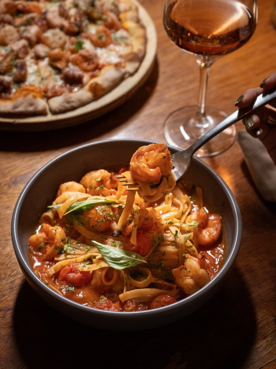 Shrimp pasta in tomato sauce, next to a glass of rosé wine.