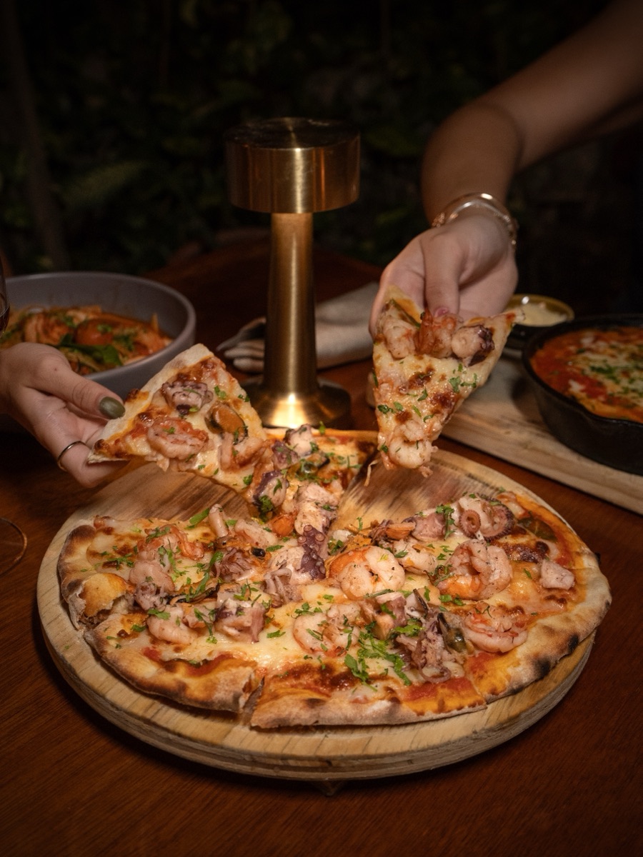 Seafood pizza shared at the table, hands reaching for slices.