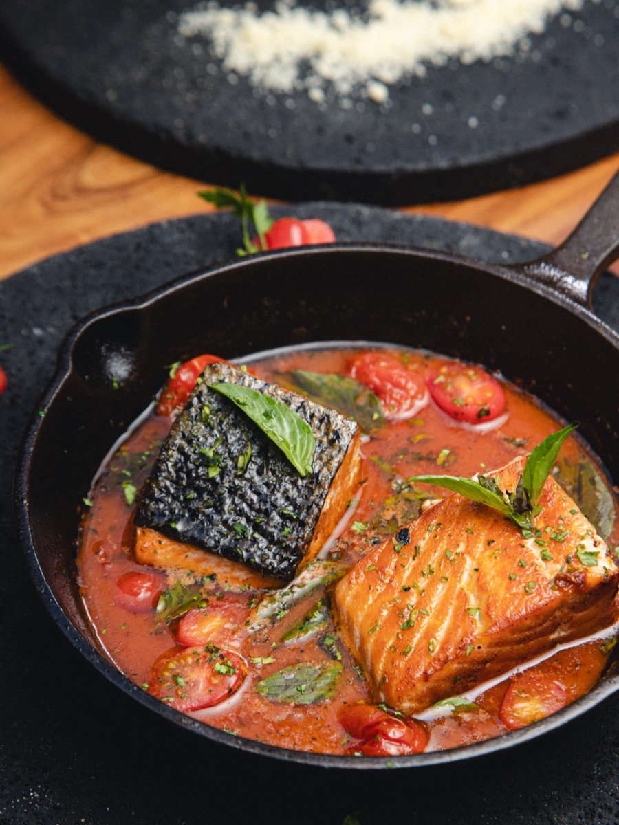 Pan-seared salmon in a cast-iron skillet, with cherry tomatoes and basil.