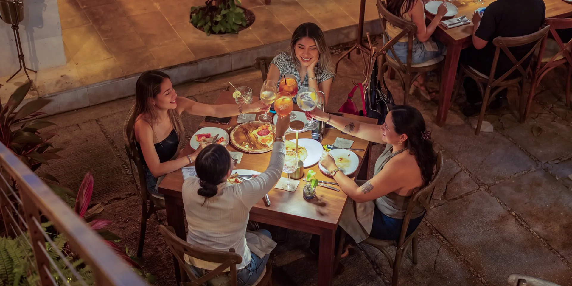 Four friends raising their glasses at a table on Mar Di Vino's patio at night